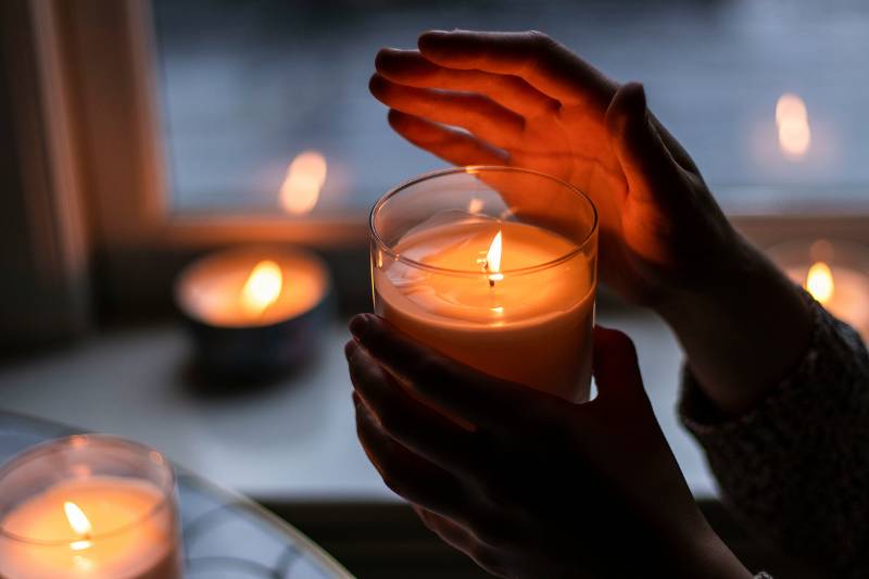 Hands warming around a lit candle